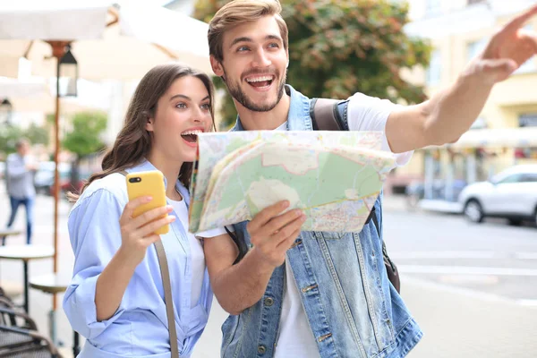 屋外に立っている間に地図と笑顔を保持する美しい若いカップル. — ストック写真