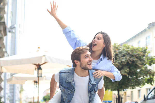 Guapo joven hombre llevando joven atractiva mujer en hombros mientras pasar tiempo juntos al aire libre. — Foto de Stock