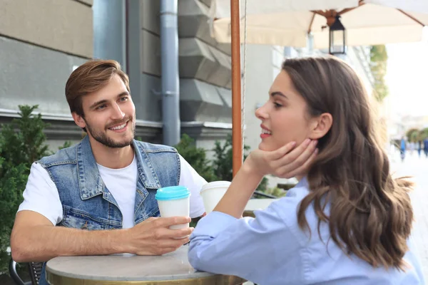 カフェテーブルに座っている間にコーヒーを飲む愛の魅力的な若いカップル屋外. — ストック写真