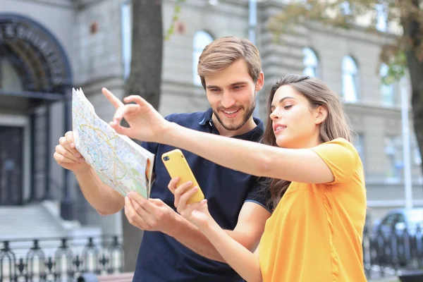 屋外に立っている間に地図と笑顔を保持する美しい若いカップル. — ストック写真