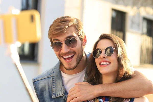 Hermosa pareja joven y encantadora caminando por las calles de la ciudad, abrazándose mientras se toma una selfie. —  Fotos de Stock