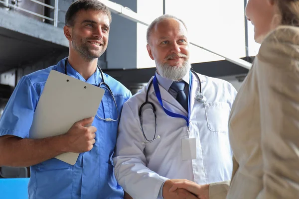 Dos médicos y una paciente que se dan la mano antes de la consulta en el consultorio de un centro médico moderno . — Foto de Stock