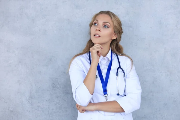 Concentrated pretty doctor with hanf on chin posing over grey background. — Stock Photo, Image