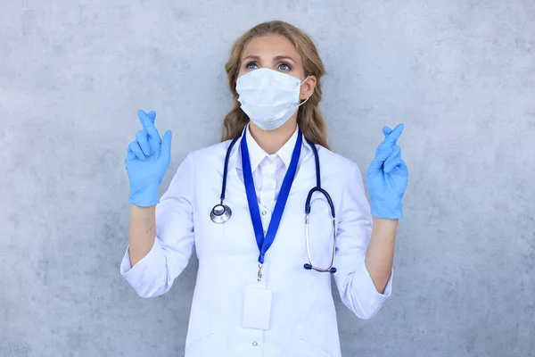 Médico femenino con dedos cruzados aislados sobre fondo gris . — Foto de Stock