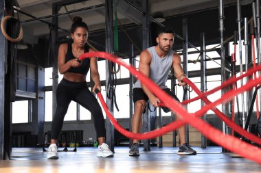 Savaş halatıyla atletik genç çift spor salonunda egzersiz yapıyor..