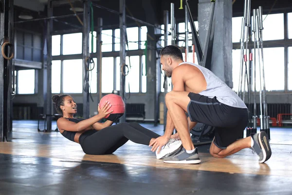 Entrenador ayudando a las jóvenes a hacer ejercicios abdominales en el gimnasio. — Foto de Stock