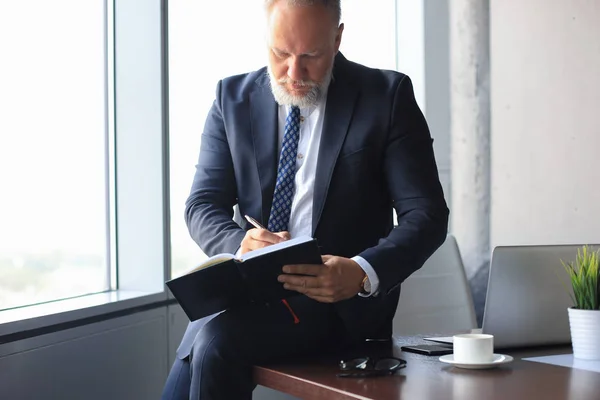Focado homem de negócios maduro trabalhando e tomando notas em seu escritório moderno. — Fotografia de Stock