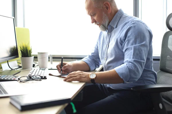 Uomo d'affari maturo cerca e analizza il documento nel suo ufficio moderno al lavoro. — Foto Stock