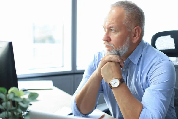 Fokuserad mogen affärsman djupt i tanken när du sitter vid ett bord i moderna kontor. — Stockfoto