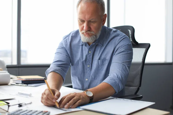 Bello sguardo architetto maturo disegno qualcosa mentre si lavora in ufficio. — Foto Stock