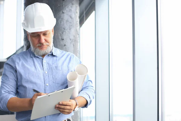 Confident mature business man in hardhat holding blueprint while standing indoors. — Stockfoto