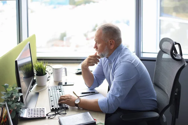 Fokuserad mogen affärsman djupt i tanken när du sitter vid ett bord i moderna kontor. — Stockfoto