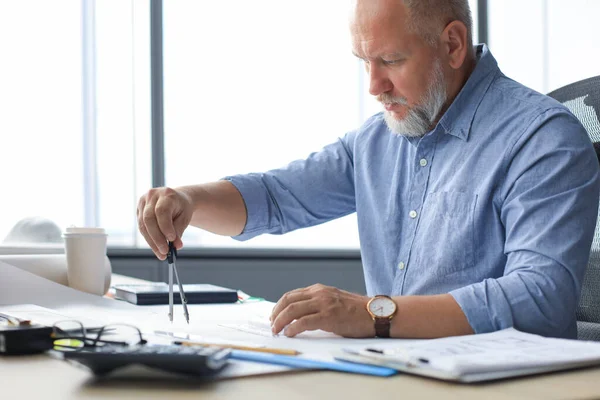 Συγκεντρωμένη ώριμη επιχείρηση άνθρωπος δουλεύοντας με πυξίδα σχεδιάζοντας ενώ κάθονται στο σύγχρονο χώρο εργασίας. — Φωτογραφία Αρχείου