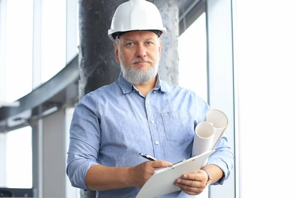 Confident mature business man in hardhat holding blueprint while — Stockfoto