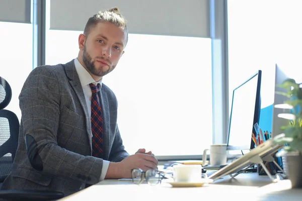 Hombre de negocios moderno mirando a la cámara mientras está sentado en la oficina . — Foto de Stock