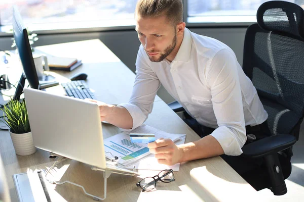 Joven hombre de negocios moderno analizando datos utilizando el ordenador portátil mientras trabaja en la oficina. — Foto de Stock