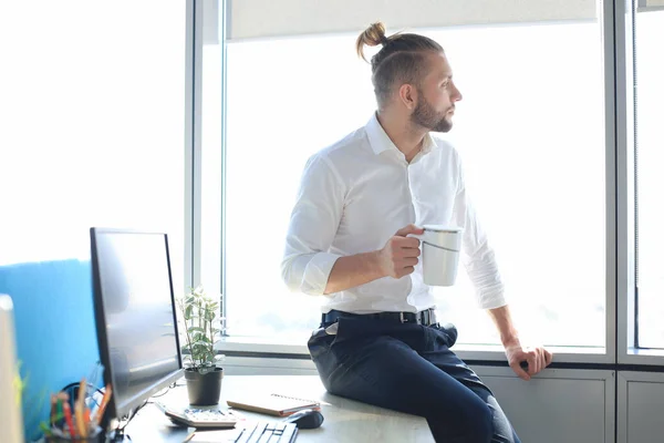 Goed uitziende jonge zakenman die koffie drinkt terwijl hij op kantoor zit. — Stockfoto