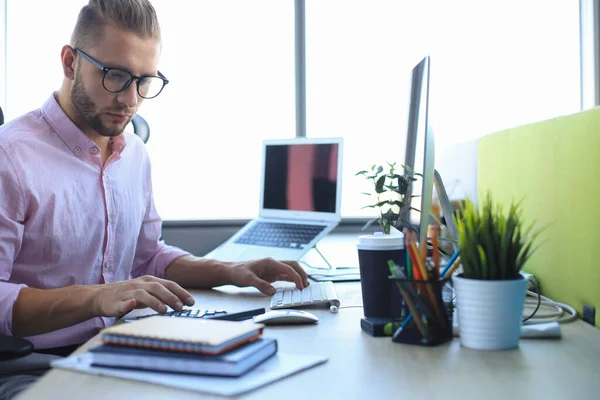 Figyelmes fiatal üzletember ingben, aki számítógéppel dolgozik, miközben az irodában ül.. — Stock Fotó
