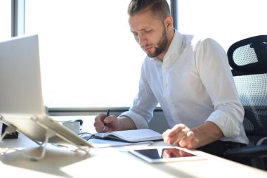 Genç modern iş adamı ofiste çalışırken dizüstü bilgisayarla veri analiz ediyor..