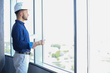 Ofisin penceresinde dikilirken planlarını inceleyen tişörtlü, kendinden emin genç bir iş adamı..