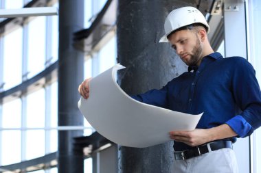 Kendine güvenen genç işadamı elinde planlar tutarken ve evin içinde onu incelerken..