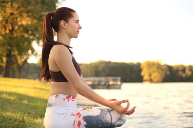 Young pretty woman in lotus pose in green park.