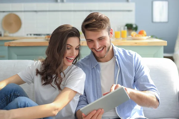 Pareja joven viendo contenido multimedia en línea en una tableta sentada en un sofá en la sala de estar. —  Fotos de Stock