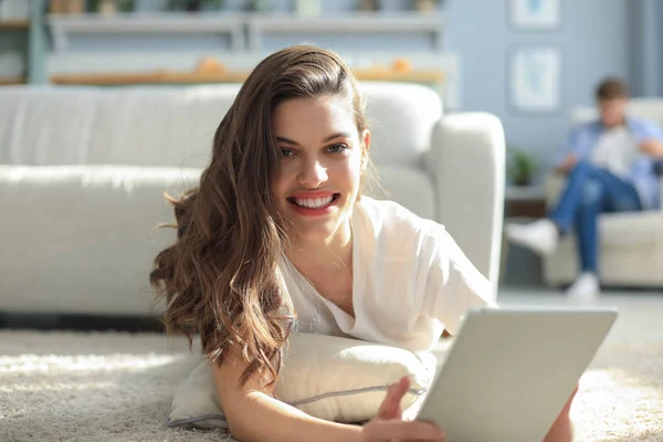 Sonriendo hermosa mujer usando el ordenador portátil con el hombre borroso en el fondo en casa . —  Fotos de Stock