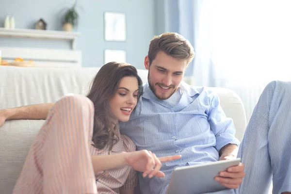 Jovem casal de pijama assistindo conteúdo de mídia online em um tablet sentado no chão na sala de estar. — Fotografia de Stock