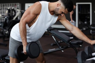 Formda ve kaslı adam dambıllarla antrenman yapıyor.