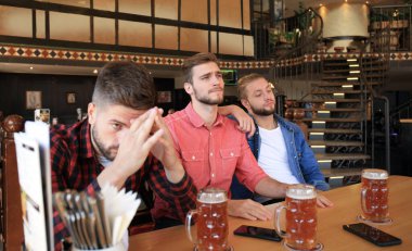 Gündelik kıyafetler içinde üç adam futbol için tezahürat ve barda bar tezgahında otururken bira şişeleri tutarak