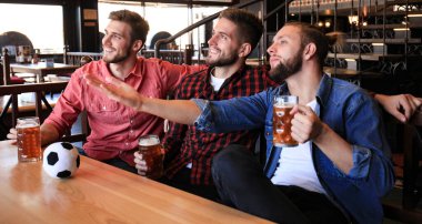 Gündelik kıyafetler içinde üç adam futbol için tezahürat ve barda bar tezgahında otururken bira şişeleri tutarak