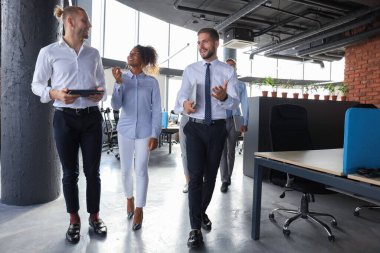 Bir grup modern iş adamı ofis koridorunda dururken konuşuyor ve gülümsüyor.
