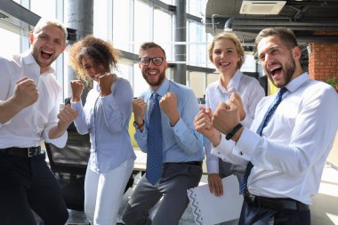 Beş mutlu modern iş adamları kollarını kaldırdı tutmak ve büyük ofiste dururken sevinçli ifade