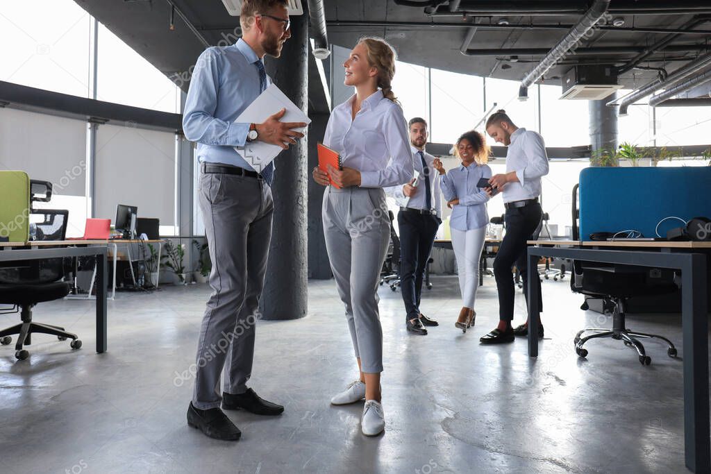 Group of modern business people are talking and smiling while standing in the office hallway