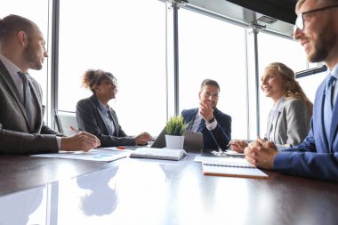 Modern ofiste çalışırken bir şeyleri gülümseyen ve tartışan formalgiyimli bir grup genç modern insan.