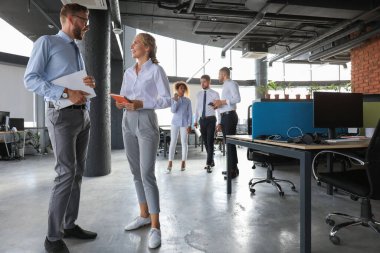 Bir grup modern iş adamı ofis koridorunda dururken konuşuyor ve gülümsüyor.