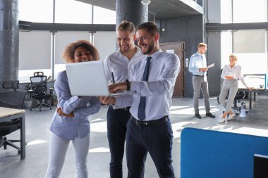 Modern iş adamları grubu ofis koridorunda dururken dizüstü bilgisayar ve gülümseyerek çalışıyoruz