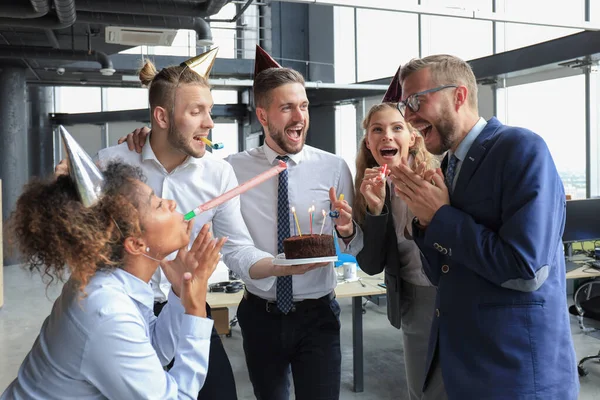 Happy business team with birthday cake are greeting colleague at office party