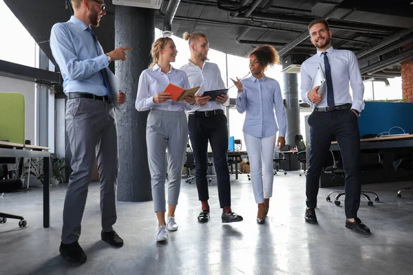 Сучасні бізнесмени обговорюють бізнес і посміхаються під час прогулянки по офісному коридору — стокове фото