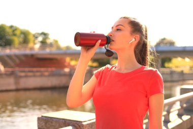 Dışarıda şişeden su içen genç, çekici, yorgun bir sporcunun resmini çek.