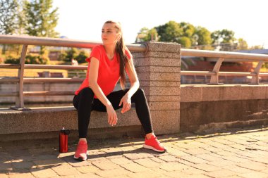 Spor giyim çekici genç kadın açık havada otururken bir mola