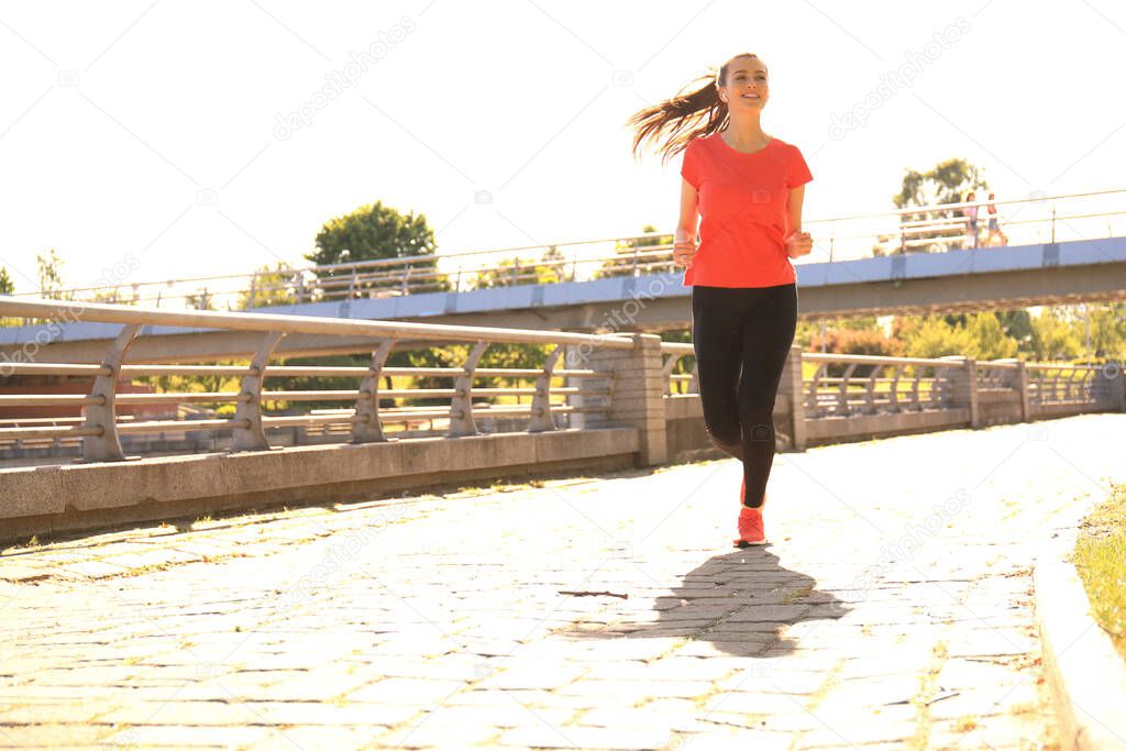 Beautiful young woman in sports clothing running while exercising outdoors