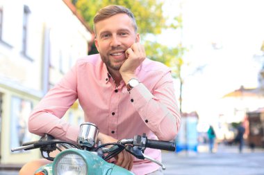 Yakışıklı adam bir tatil bağlamda bir scooter üzerinde poz. Sokak moda ve stil