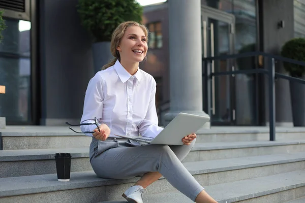 Beautiful excited business woman sitting near business center and using laptop
