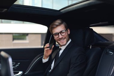Yakışıklı işadamı arabanın arka koltuğunda dizüstü bilgisayar ile oturan telefon ile konuşuyor