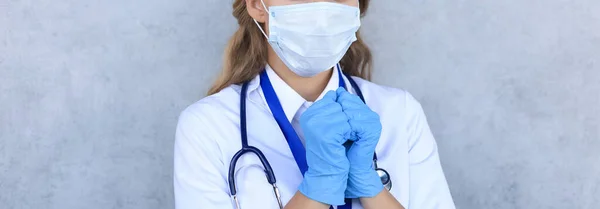 Woman doctor in a mask with closed eyes praying isolated on gray background