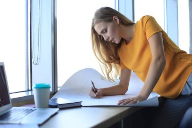 Güzel modern kadın yaratıcı ofiste çalışırken planı aşağı bir şey yazıyor.