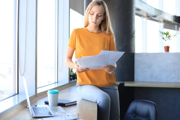 Atractiva Mujer Negocios Sosteniendo Documentos Mirándolos Mientras Está Sentada Escritorio — Foto de Stock