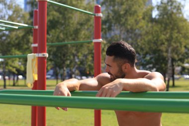 Güneşli bir günde parkta spor yaparken çıplak gövdesi dinlenen yakışıklı sporcu..